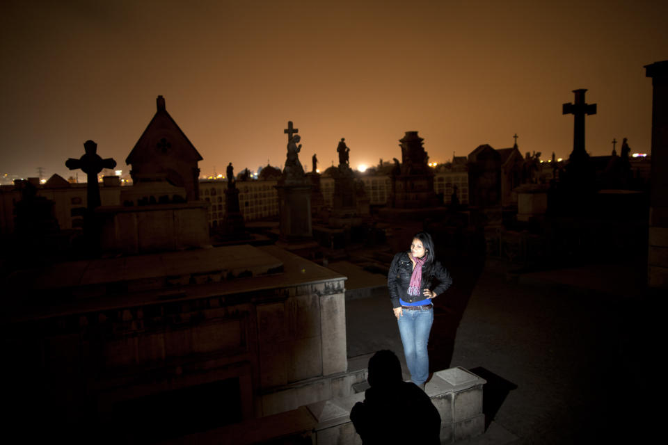 In this Sept. 20, 2012 photo, a girl poses for the picture on a tomb during a nighttime guided tour through the Presbitero Matias Maestro cemetery in Lima, Peru. Visitors to the 54-acre cemetery just 20 blocks from Lima's presidential palace, one of Latin America's oldest, are treated to tales about the people buried here in a three-hour, nighttime guided tour run by its owner, Beneficiencia de Lima (AP Photo/Rodrigo Abd)