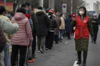 In this photo released by Xinhua News Agency, a volunteer wearing a face mask to protect from the coronavirus uses a loud speaker to give advise to masked residents as they line up for the coronavirus test during a mass testing in north China's Tianjin municipality, Sunday, Jan. 9, 2022. Tianjin, a major Chinese city near Beijing has placed its 14 million residents on partial lockdown after 41 children and adults tested positive for COVID-19, including at least two with the omicron variant. (Sun Fanyue/Xinhua via AP)