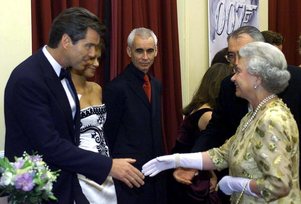 Britain's Queen Elizabeth II is greeted by Irish actor Pierce Brosnan (L) as she arrives for the World Premiere of the new James Bond film 'Die Another Day' directed by New Zealand's Lee Tamahori (C) at the Royal Albert Hall in central London, 18 November 2002. The film opening 22 November stars also US academy-award winner Halle Berry (2nd L behind Brosnan).         (Photo credit should read TIM CLARKE/AFP/GettyImages)