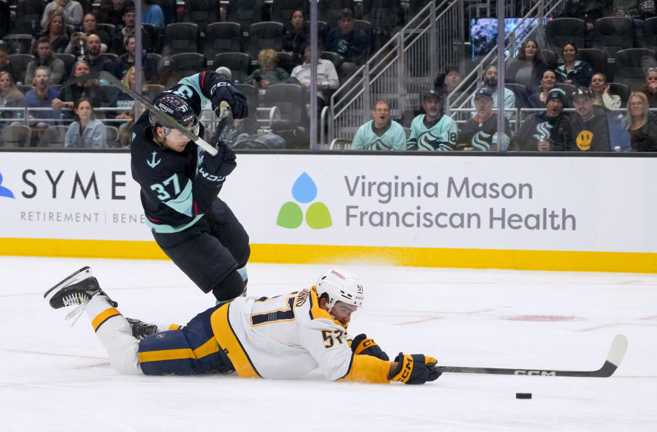 Nashville Predators defenseman Dante Fabbro (57) reaches for the puck as he falls next to Seattle Kraken center Yanni Gourde (37) during the second period of an NHL hockey game Thursday, Nov. 2, 2023, in Seattle. (AP Photo/Lindsey Wasson)