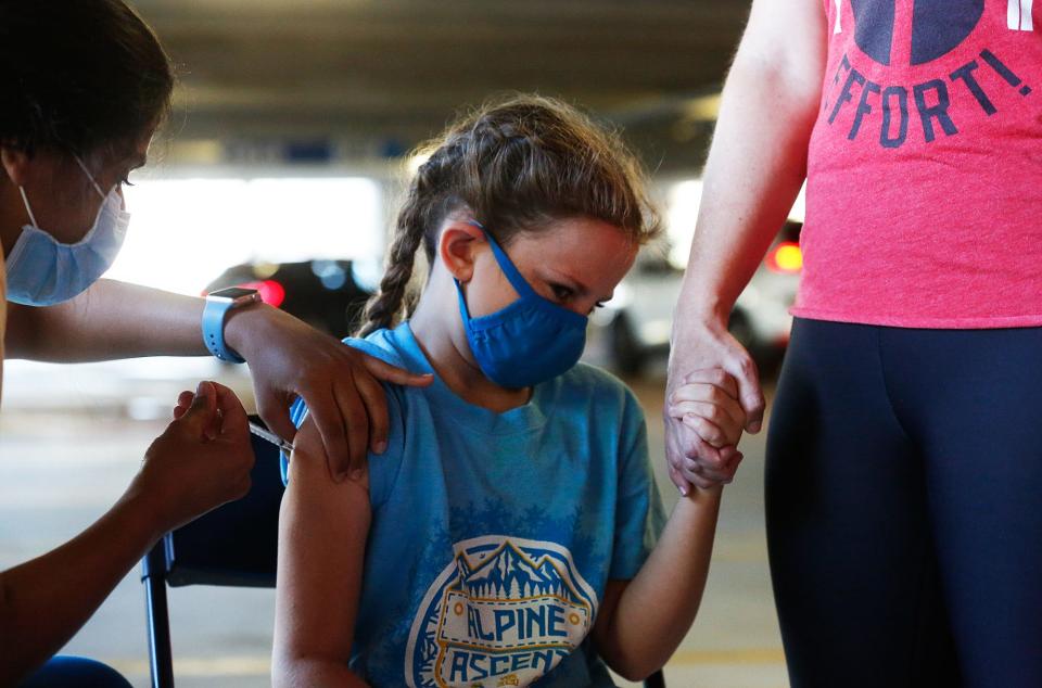 Hannah Sullivan, 8, holds her parent's hand as she receives a dose of the Pfizer BioNTech vaccine at a pop-up clinic in the parking garage outside the Phillips Center in Gainesville on Wednesday.