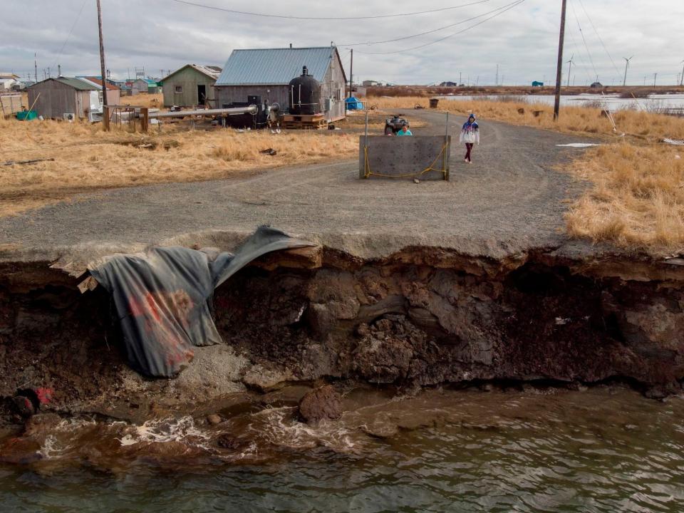 A gravel road abruptly ends crumbling into running water 2 feet below in rural setting with a few homes.