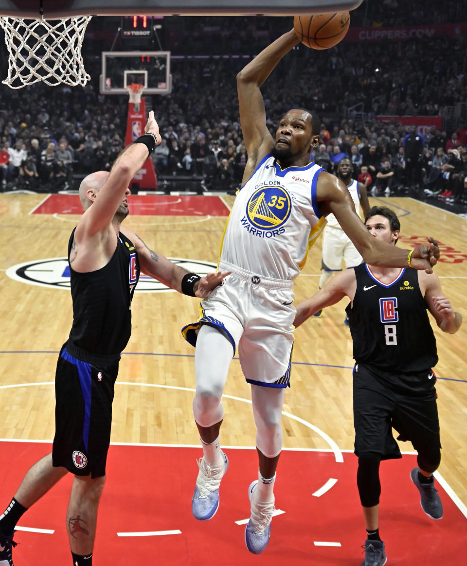 Golden State Warriors forward Kevin Durant, center, goes up for a dunk as Los Angeles Clippers center Marcin Gortat, left, and forward Danilo Gallinari defend during the first half of an NBA basketball game Friday, Jan. 18, 2019, in Los Angeles. (AP Photo/Mark J. Terrill)