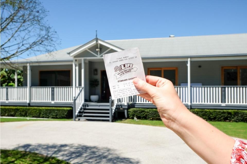 lottery player holds set for life ticket in front of house