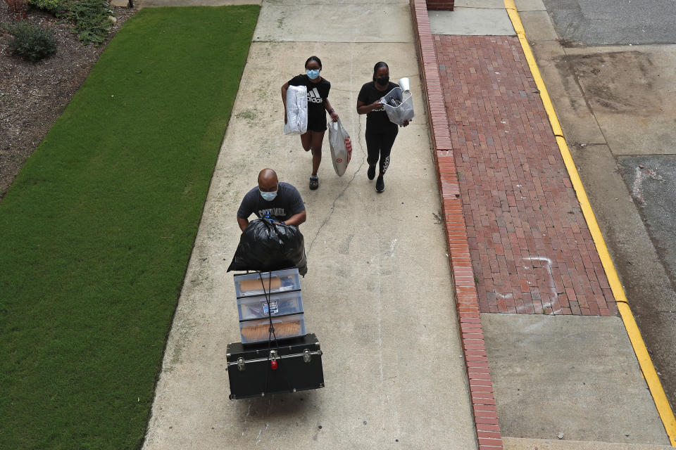 A family carries their belongings while college students begin moving in for the fall semester at N.C. State University in Raleigh, N.C., Friday, July 31, 2020. The first wave of college students returning to their dorms aren’t finding the typical mobs of students and parents. At N.C. State, the return of students was staggered over 10 days and students were greeted Friday by socially distant volunteers donning masks and face shields. (AP Photo/Gerry Broome)