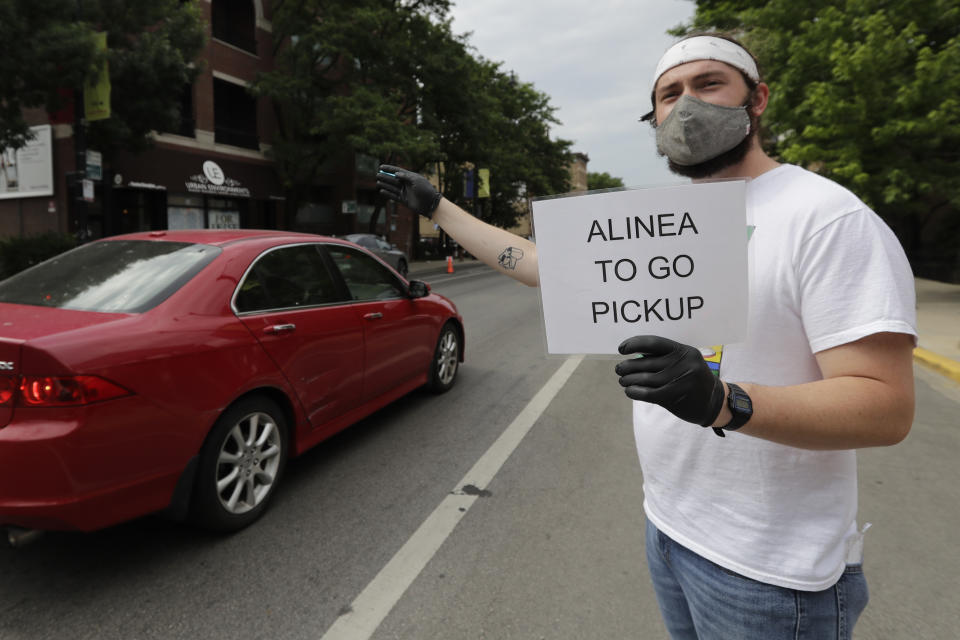 Cal Barnett, a staffer from Alinea restaurant, holds a sign for carryout customers in Chicago, Saturday, June 20, 2020. Due to the coronavirus Alinea shifted to carryout on March 17. Since then, it has served 82,000 meals, said Nick Kokonas, the restaurant's co-owner. (AP Photo/Nam Y. Huh)