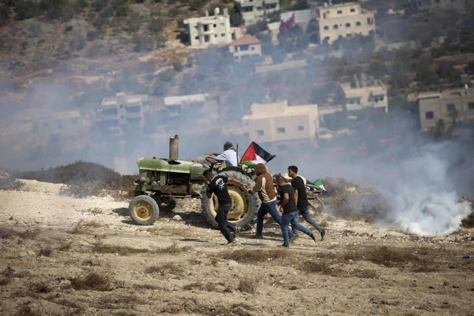 Palestinians run from tear gas fired by Israeli forces during clashes as they protest against Israeli Jewish settlements in Asira al-Qibliya near the West Bank city of Nablus, Friday, Sept. 25, 2020. (AP Photo/Majdi Mohammed)