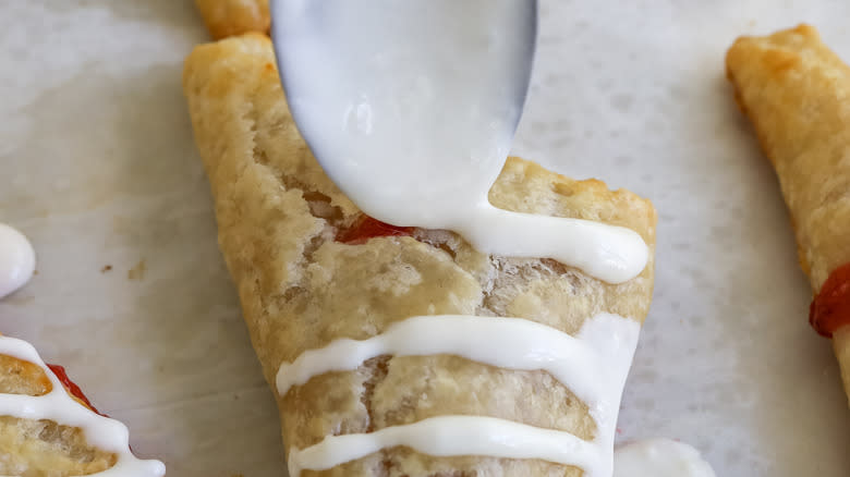 glaze being drizzled with a spoon onto baked turnovers