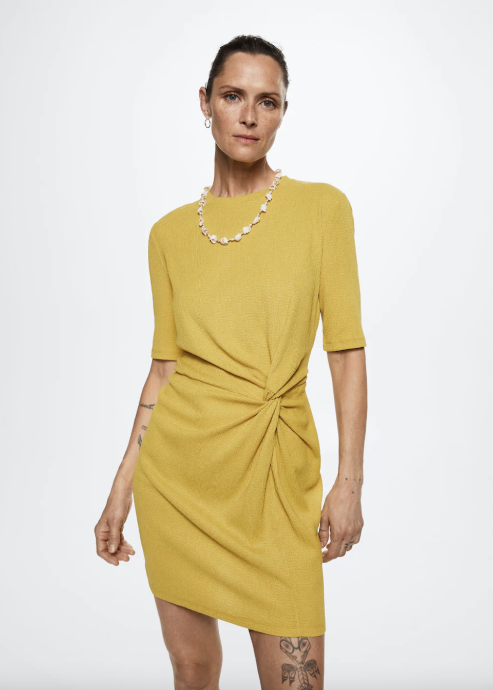 woman with leg tattoo wearing pearl necklace and mustard yellow Mango Ruched Detail Dress (Photo via Mango)