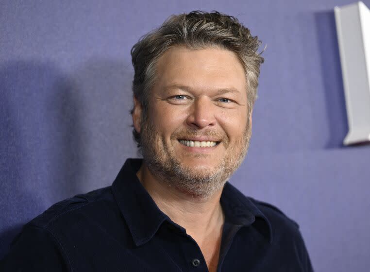 A man in a black shirt and scruffy facial hair smiles big for cameras at an event