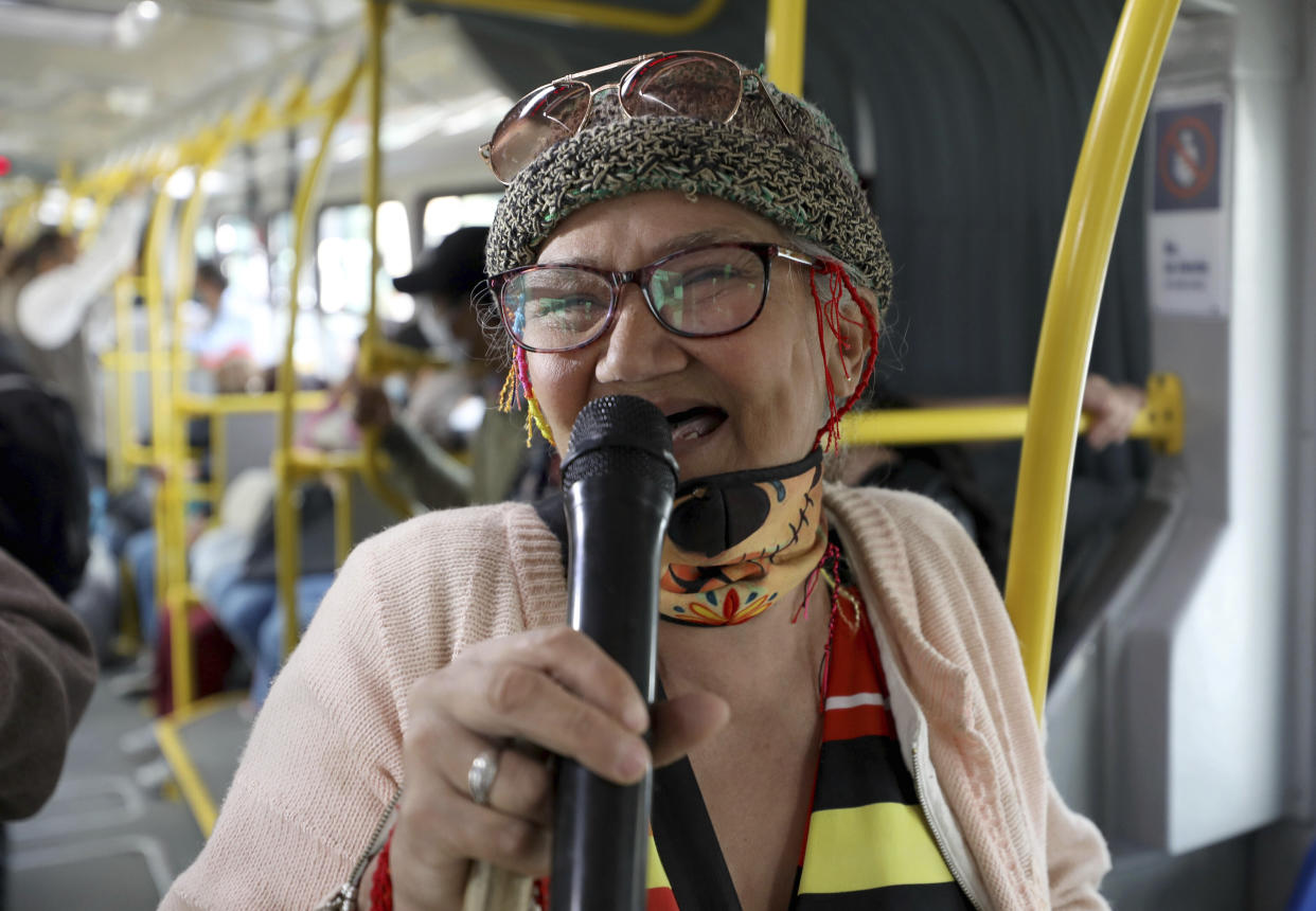 Marlene Alfonso, una abuela venezolana de 69 años que se hace llamar "Cindy sin dientes", canta sobre la vida de los migrantes de su país con la esperanza de recibir propinas de los viajeros en el Transmilenio, el sistema de autobuses públicos atestado y asotado por el crimen en Bogotá, el martes 3 de noviembre de 2020. (AP Foto/Fernando Vergara)