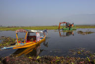 A Kashmiri boatman rows his boat as a de-weeding machine works at Dal lake in Srinagar, Indian controlled Kashmir, Tuesday, Sept. 14, 2021. Weeds, silt and untreated sewage are increasingly choking the sprawling scenic lake, which dominates the city and draws tens of thousands of tourists each year. (AP Photo/Mukhtar Khan)