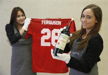 Employees pose with a bottle of "Petrus 1988" wine and a Manchester United Retro Champions League shirt from 1999 signed by retired boss Alex Ferguson, at Christie's auction house in London April 14, 2014. REUTERS/Luke MacGregor