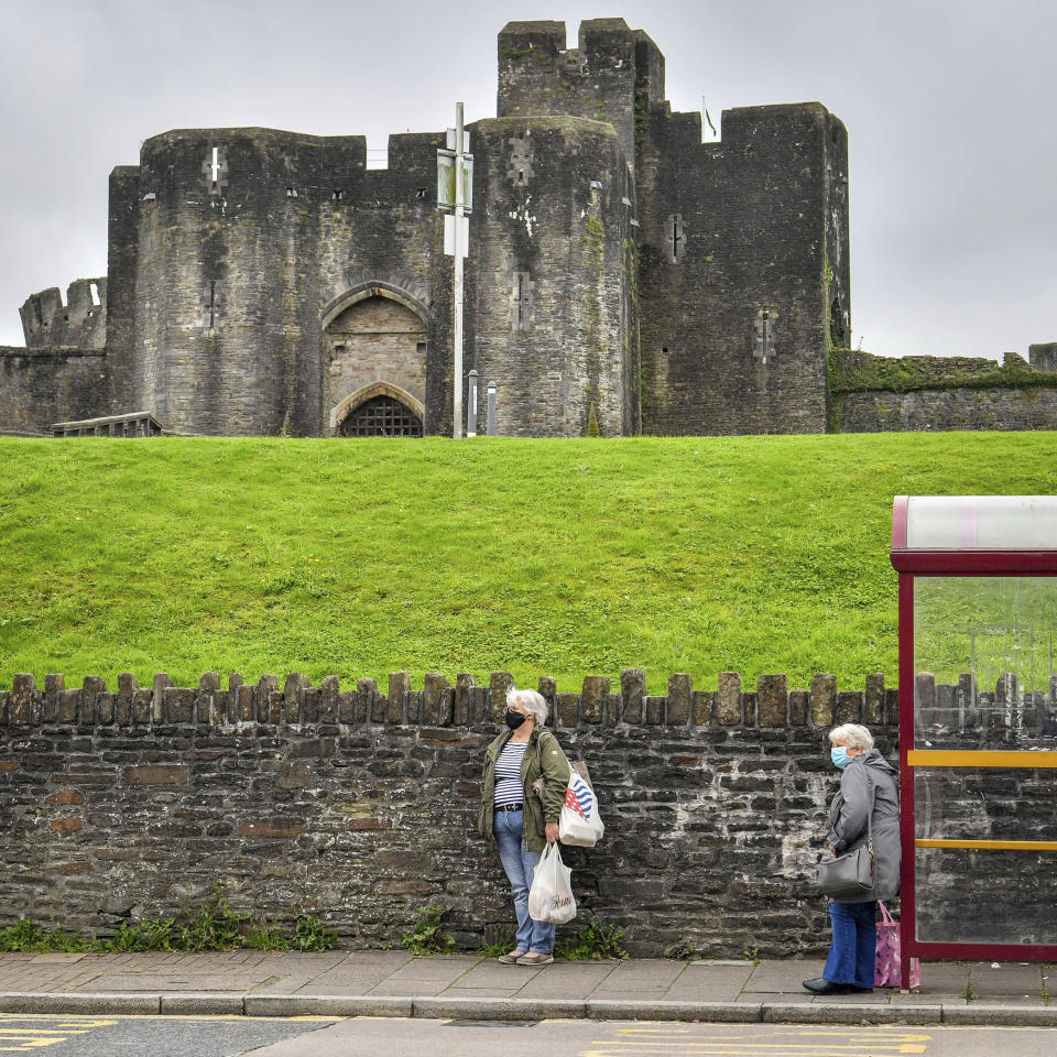 People wear masks as they wait for a bus beside Caerphilly castle, a day after the county borough of Caerphilly began a local lockdown following a "significant rise" in coronavirus cases, in Caerphilly, South Wales, Wednesday, Sept. 9, 2020. (Ben Birchall/PA via AP)