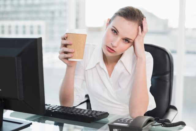 Stressed businesswoman holding disposable cup looking at camera in her office