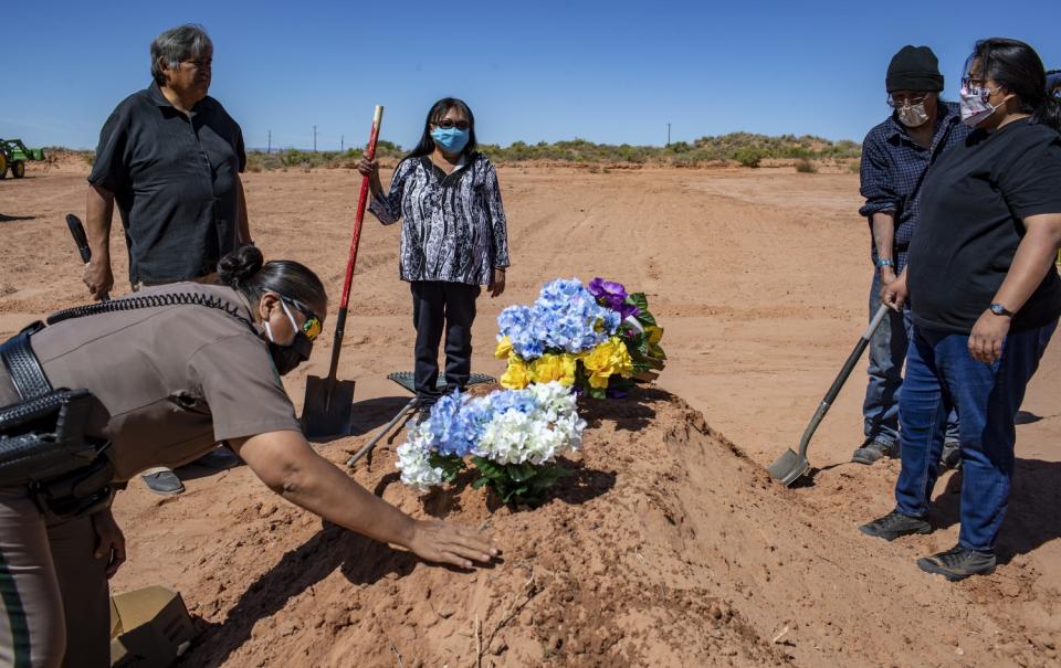 Carlita Bergen, center, holds a shovel as Officer Carolyn Tallsalt smooths dirt over COVID-19 victim Arnold Billy's grave