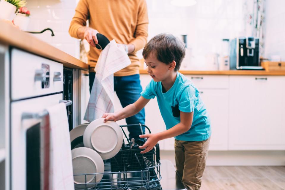 boy loading dishwasher with father