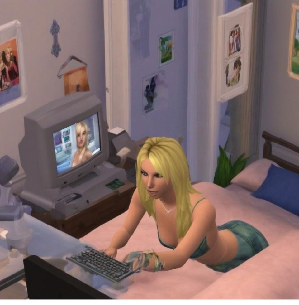 Sims character with blonde hair using a computer in a bedroom decorated with posters