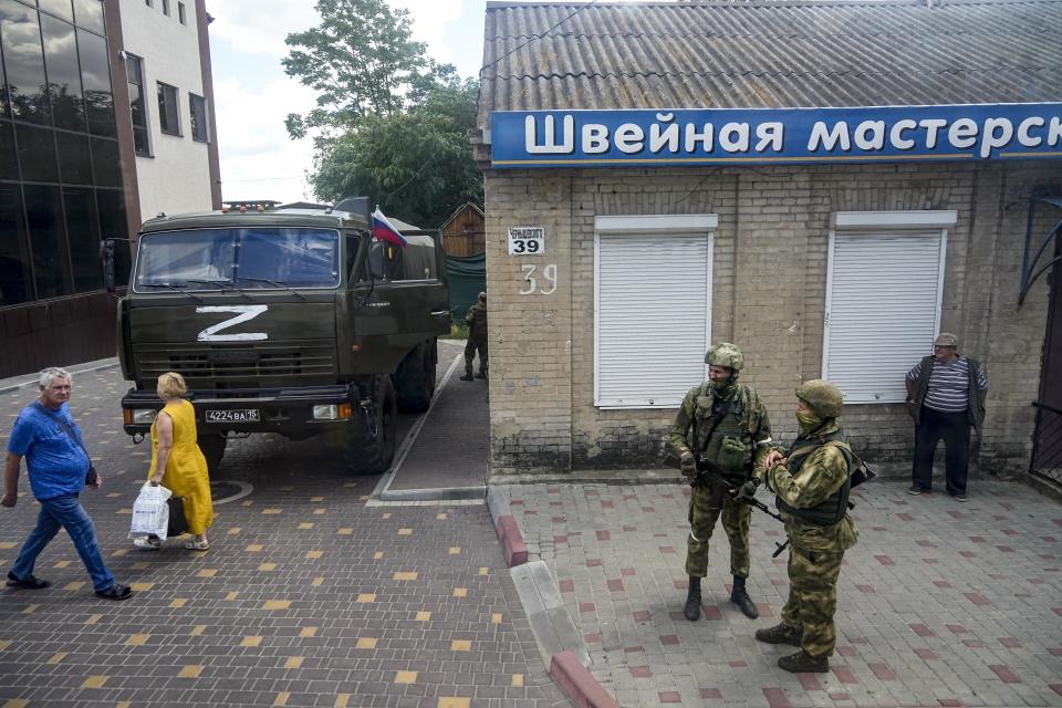 FILE - Russian soldiers guard an office for Russian citizenship applications as their military truck is parked nearby, in Melitopol, south Ukraine, on July 14, 2022. As Russians seized parts of eastern and southern Ukraine in the 8-month-old war, mayors, civilian administrators and others, including nuclear power plant workers, say they have been abducted, threatened or beaten to force their cooperation. In some instances, they have been killed. Human rights activists say these actions could constitute a war crime. (AP Photo, File)
