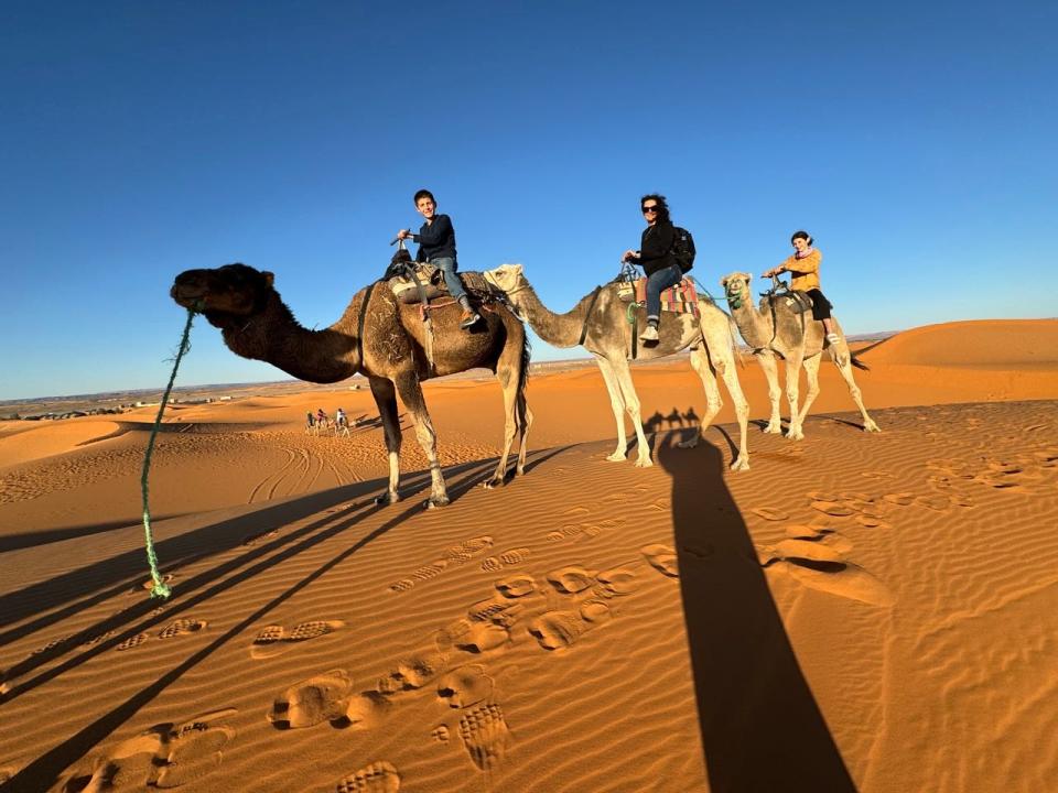 Three people on camels in Sahara desert sands 