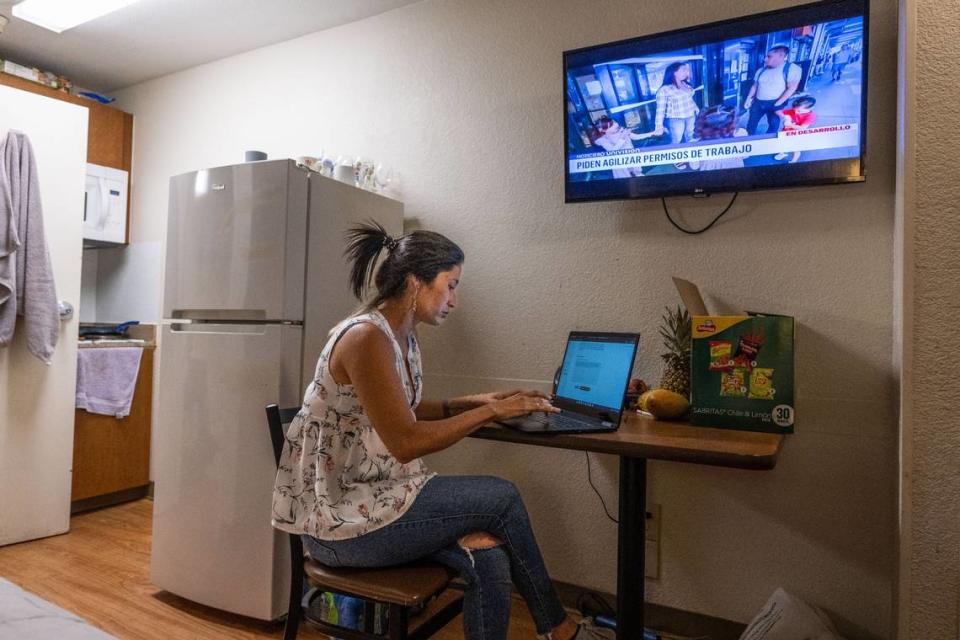 Aura, 31, of Colombia, looks at the website to apply for asylum in August 2023, as a national Spanish television network runs a story on migrants in New York. Aura, who arrived in Sacramento months before on a plane chartered by Florida's governor, and other migrants struggle with the decision to seek asylum as it could potentially be the start of a deportation order.