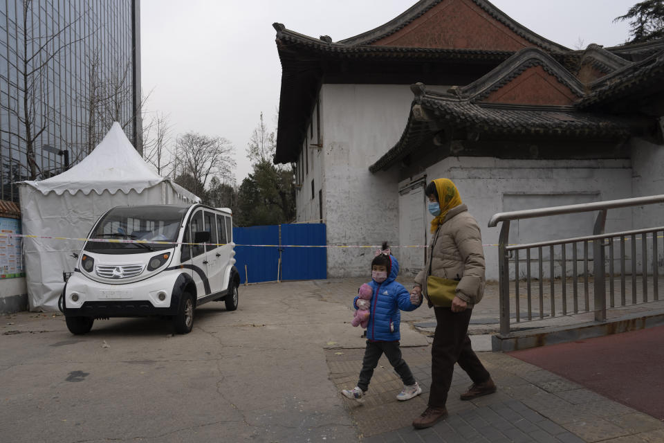 A woman and child wearing masks walk near a closed off area in Beijing, Friday, Dec. 2, 2022. More cities eased restrictions, allowing shopping malls, supermarkets and other businesses to reopen following protests last weekend in Shanghai and other areas in which some crowds called for President Xi Jinping to resign. (AP Photo/Ng Han Guan)