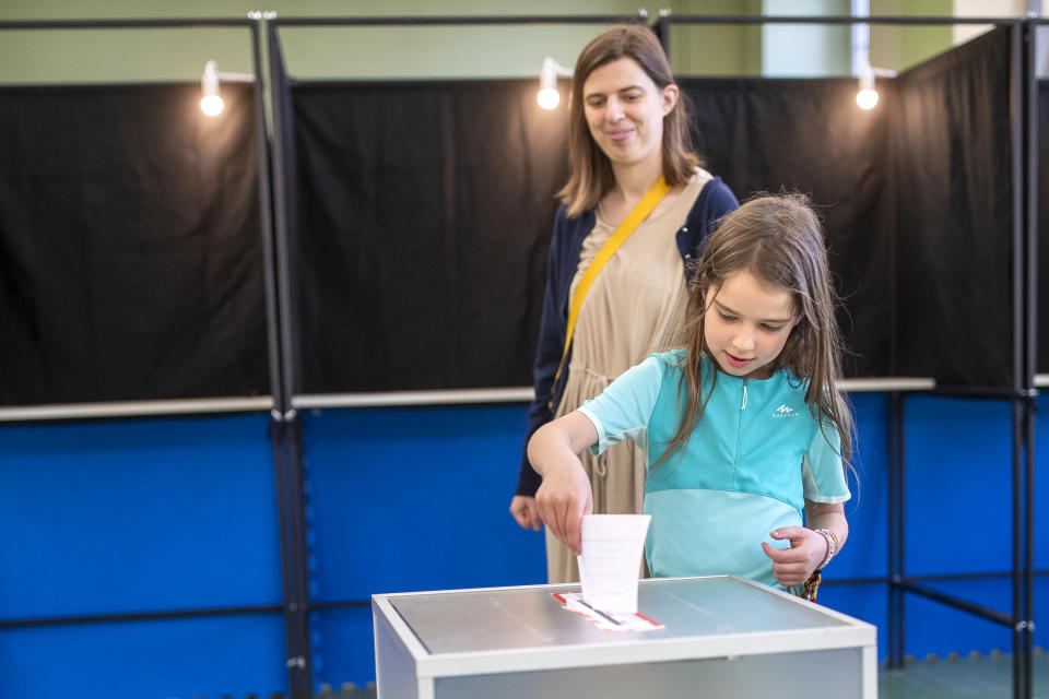 A gild puts a ballot slip in a box for a woman, at a polling station during the second round of voting in presidential elections, in Vilnius, Lithuania, Sunday, May 26, 2024. Lithuania's incumbent president won the most votes in the first round with 44% of the votes but he still faces a runoff against the country's prime minister. (AP Photo/Mindaugas Kulbis)