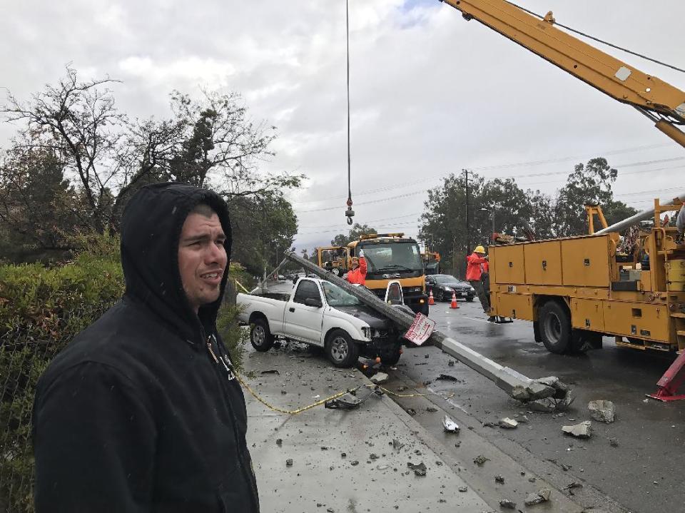 Los Angeles Iron Worker Local 433 member Robert Gutierrez stands under the rain by his truck after it hydroplaned off the road Friday, Dec. 16, 2016, off Los Feliz Blvd in Los Angeles. Rockslides caused by drenching rains have forced closure of about 36 miles of Highway 1 on California's Central Coast. A late fall storm has drenched California, causing some mud flows, roadway flooding and traffic snarls as it takes parting shots at the south end of the state. (AP Photo/Damian Dovarganes)