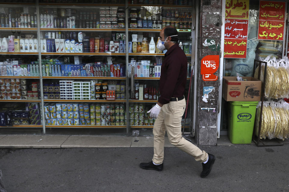 A man wearing a face mask and gloves to protect against the new coronavirus walks past a grocery in northern Tehran, Iran, Saturday, April 4, 2020. In the first working day after Iranian New Year holidays authorities have allowed some government offices and businesses to re-open with limited working hours, when schools, universities, and many businesses still are ordered to be closed aimed to prevent the spread of the virus. (AP Photo/Vahid Salemi)