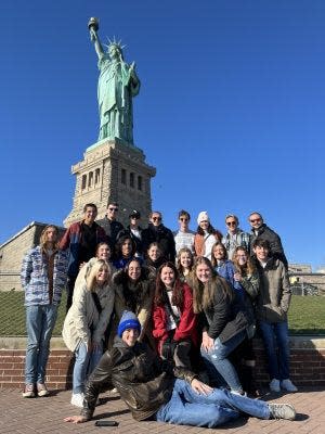 A group of Pride members stands in front of the Statue of Liberty.