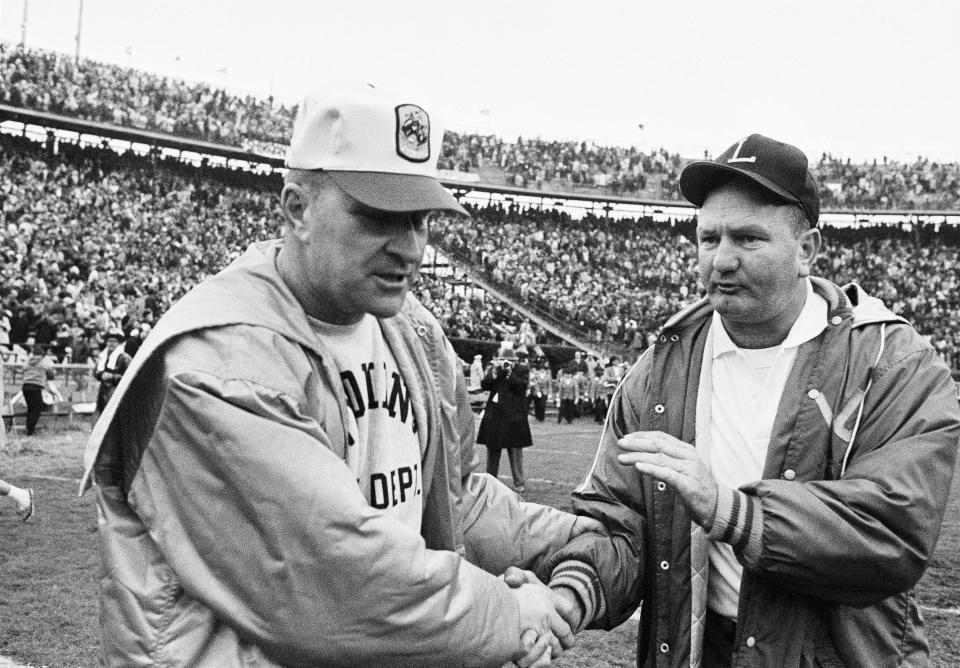 FILE - In this Jan. 1, 1968, file photo, LSU coach Charlie McClendon, right, pats the hand of Wyoming coach Lloyd Eaton in the Sugar Bowl at New Orleans. The University of Wyoming is welcoming eight former football players back on campus half a century after a racist episode gutted their team. University officials plan to unveil a plaque commemorating the Black 14 athletes at War Memorial Stadium on Friday, Sept. 13, 2019. Eaton dismissed the 14 black players after they asked Eaton if they could wear black armbands to protest racism. Black 14 members say their biggest disappointment is not hearing Eaton explain himself. Eaton died in 2007. (AP Photo/File)