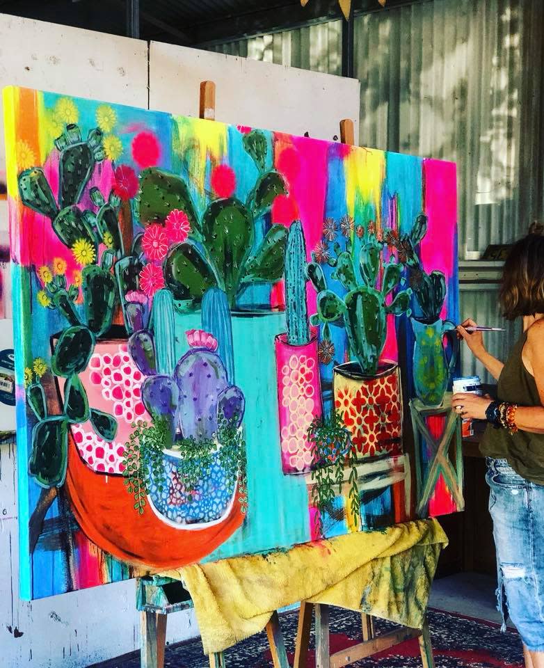 A large canvas painting of cacti in bright primary colours in worked on by Jacinta Haycock