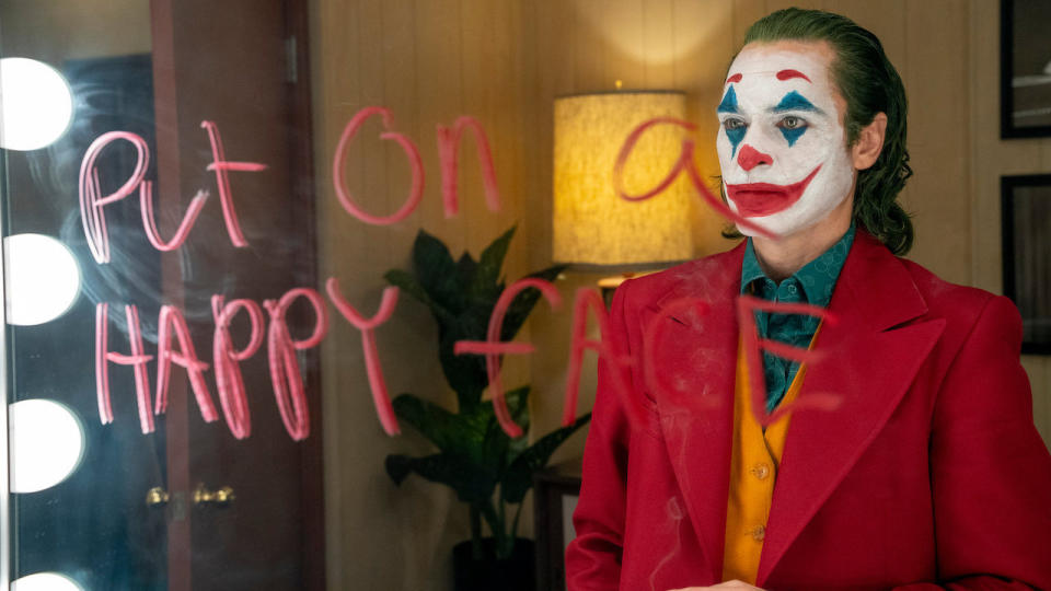 Joaquin Phoenix as Arthur Fleck in clown makeup and 'put on a happy face' on a mirror in red in Joker