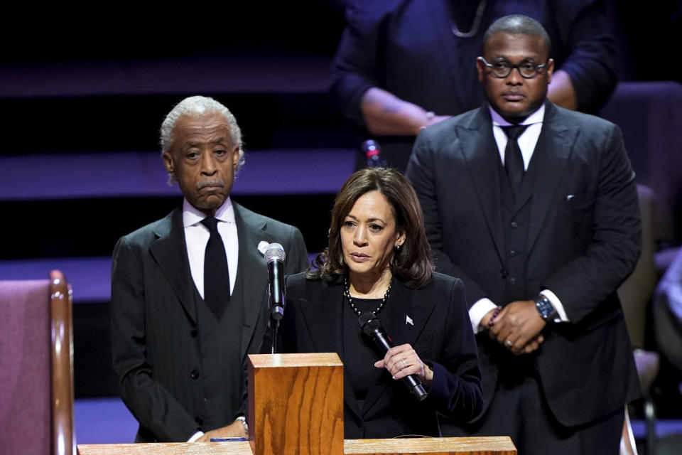 Vice President Kamala Harris at the microphone, with the Rev. Al Sharpton and the Rev. J. Lawrence Turner standing behind her looking solemn.