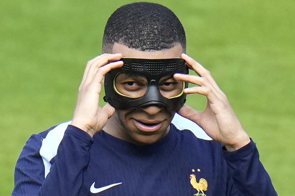 FILE - France's Kylian Mbappe gestures as he adjusts his face mask during a training session in Paderborn, Germany, on June 27, 2024. Kylian Mbappé has had more masks than goals at Euro 2024. Widely regarded as the heir to Lionel Messi and Cristiano Ronaldo as soccer's biggest icon, the France striker is struggling with his peripheral vision due to the protective face covering he has been fitted with since breaking his nose at the start of the European Championship. (AP Photo/Hassan Ammar)