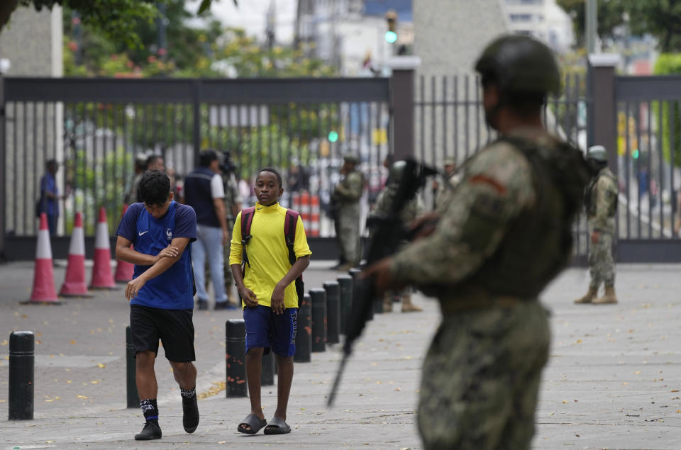 Students walk past soldiers standing guard inside a school in downtown Guayaquil, Ecuador, Friday, Aug. 18, 2023. Ecuadorians will choose a new president Sunday, less than two weeks after the South American country was shaken by the assassination of one of the candidates. (AP Photo/Martin Mejia)