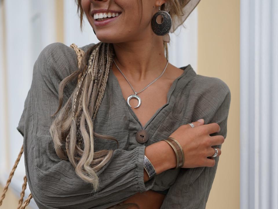 A girl in a scarf with beautiful long dreadlocks and jewelry walks on the street. Stylish hippie girl in boho clothes dances and laughs