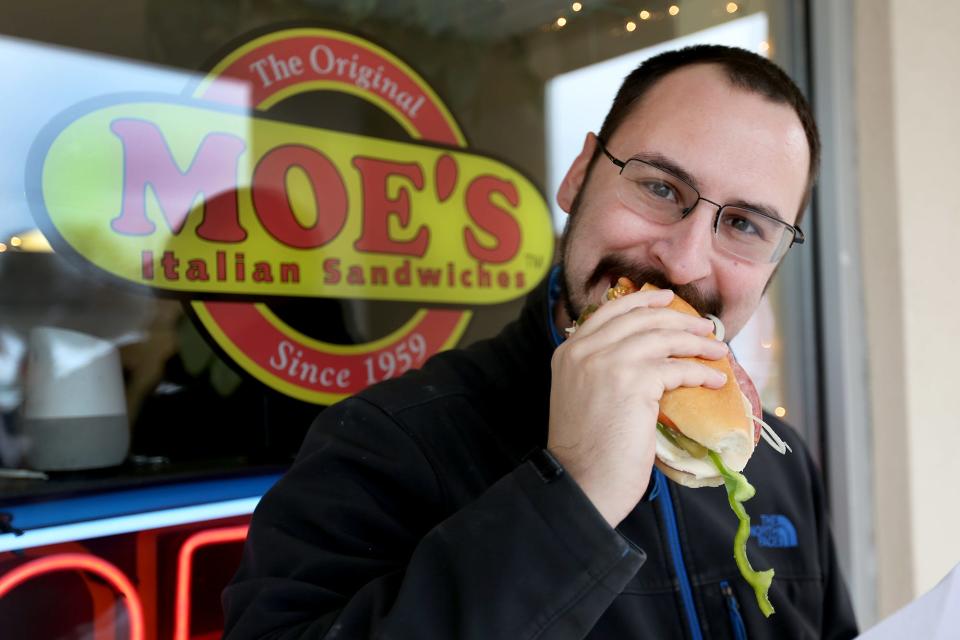 Dover resident Joshua Milas takes a bite out of his sandwich outside of the Moe’s Italian Sandwiches in Exeter on Feb. 1, 2022.