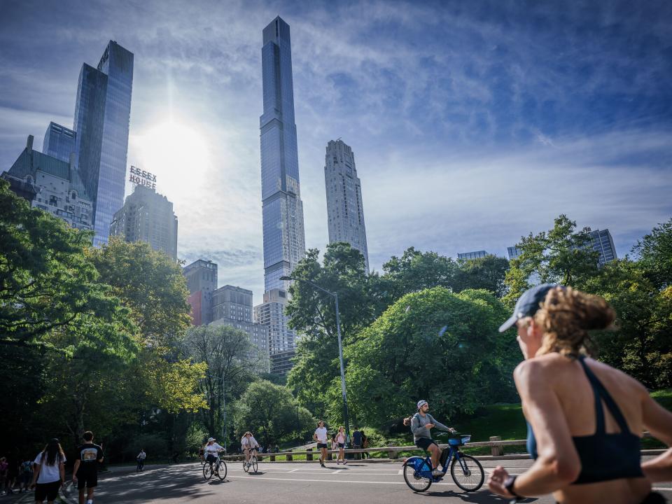 Joggers and cyclists in a park with skyscrapers in the background.