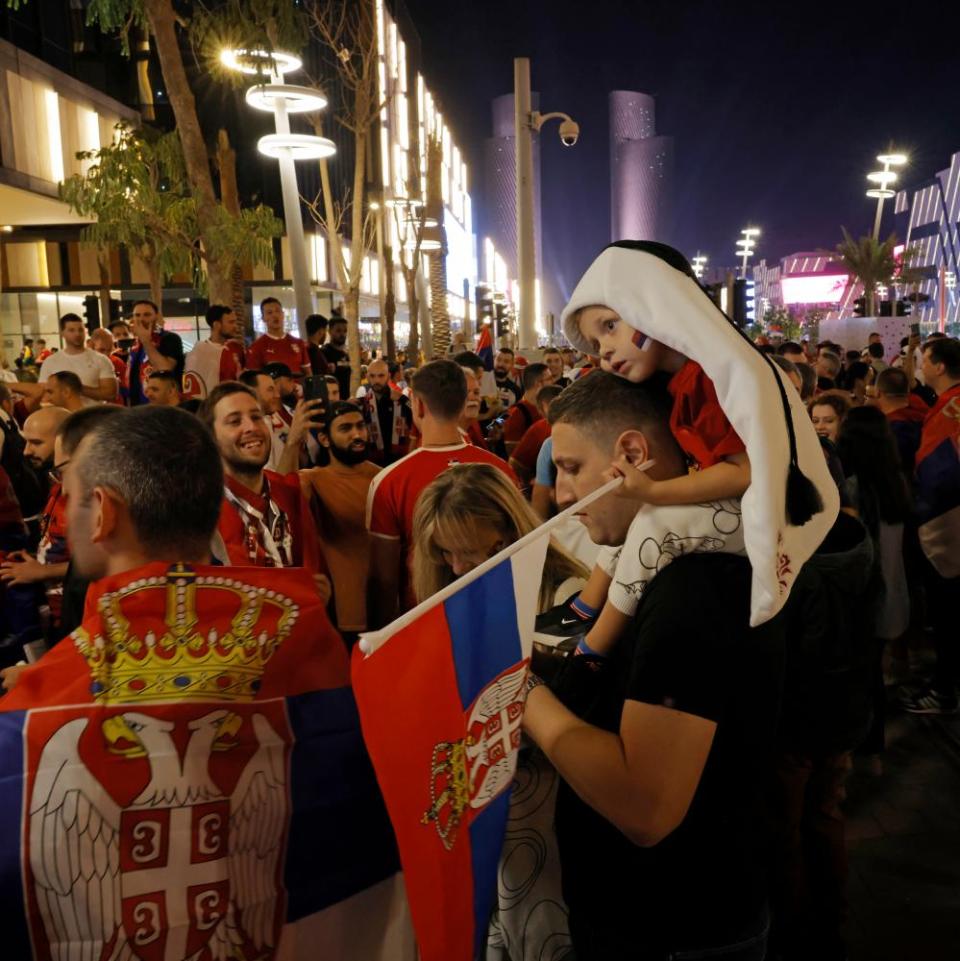 A young Serbian boy, wearing a head-dress shaped to look like the tournament mascot La’eeb, looks tired on his father’s shoulders as Serbian fans gather outside the McDonalds on Lusail Boulevard before the Brazil v Serbia World Cup match.