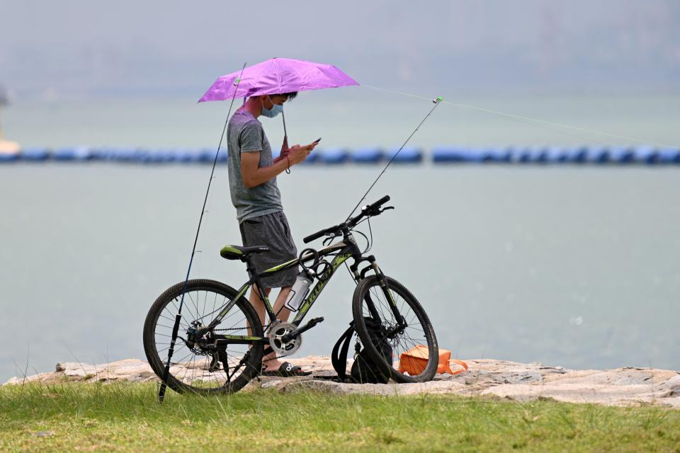 A man looks on his mobile phone while fishing along a beach in Singapore on April 13, 2021. (Photo by Roslan RAHMAN / AFP) (Photo by ROSLAN RAHMAN/AFP via Getty Images)