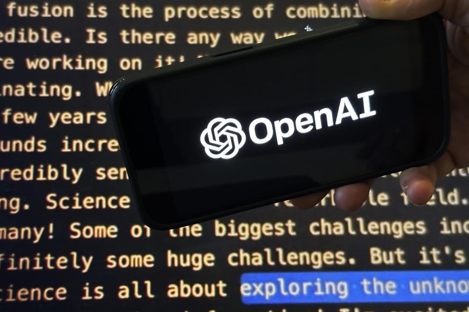 FILE - The OpenAI logo appears on a mobile phone in front of a screen showing a portion of the company website, Tuesday, Nov. 21, 2023, in New York. Sports Illustrated is the latest media company damaged by being less than forthcoming about who or what is writing its stories. The website Futurism reported that the once-grand magazine used articles with “authors” who apparently don't exist, with photos generated by AI. The magazine denied claims that some articles themselves were AI-assisted, but has cut ties with a vendor it hired to produce the articles. (AP Photo/Peter Morgan, File)