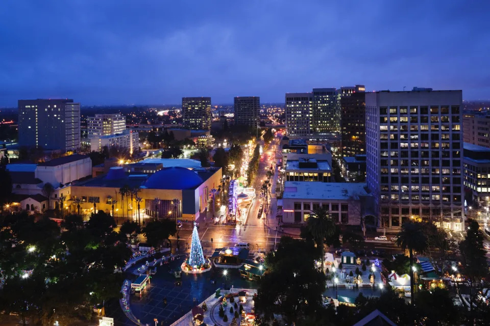 Aerial view of a cityscape at dusk with lit buildings and a Christmas tree