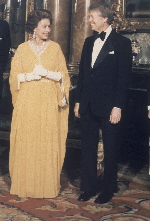The Queen embraces 1970's fashion in a golden floor-length gown while visiting with President Jimmy Carter at Buckingham Palace in May of 1977.