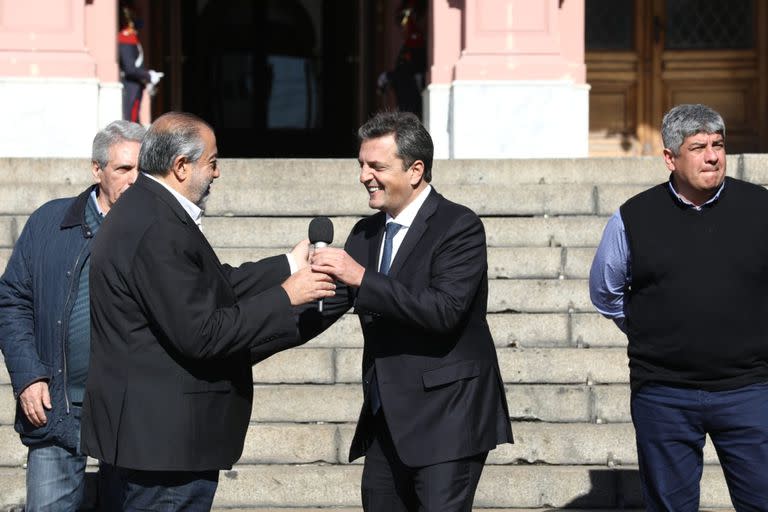 Héctor Daer le pasa el micrófono a Sergio Massa en la conferencia por el aumento del piso de ganancias, detrás están Carlos Acuña y Pablo Moyano