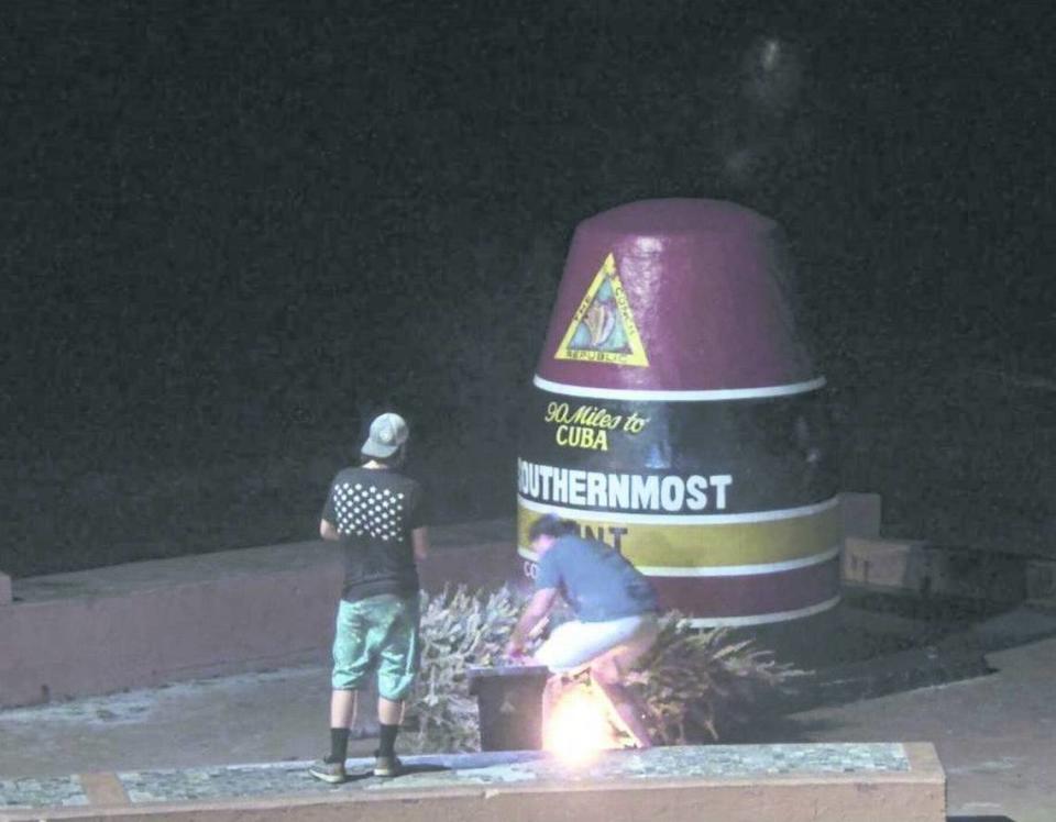 In a screenshot from a webcam, two people are seen setting a Christmas tree on fire beside the Southernmost Point buoy in Key West on Jan. 1, 2022.