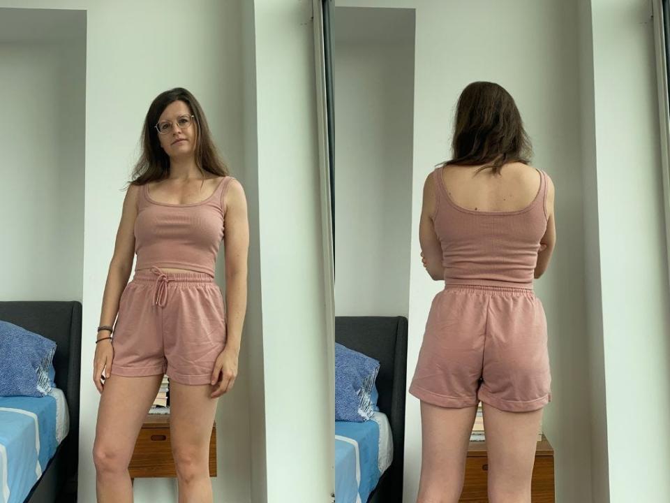 Two side by side pictures of a woman standing in a room, facing the front and back, wearing a dusty pink crop top and shorts. She has long brown hair and gold glasses.