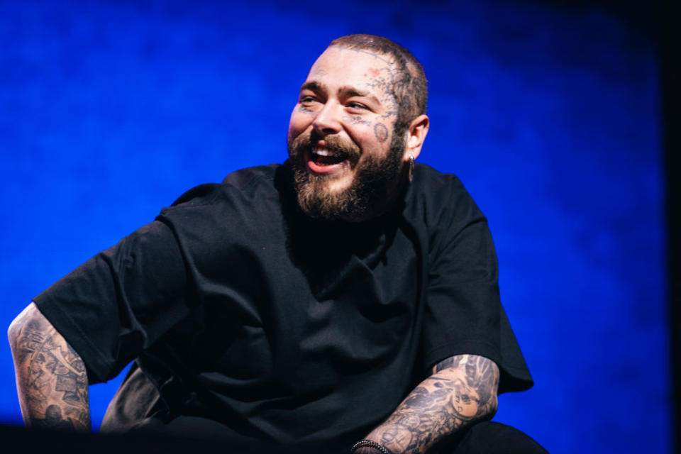 Person with tattoos smiling while seated onstage