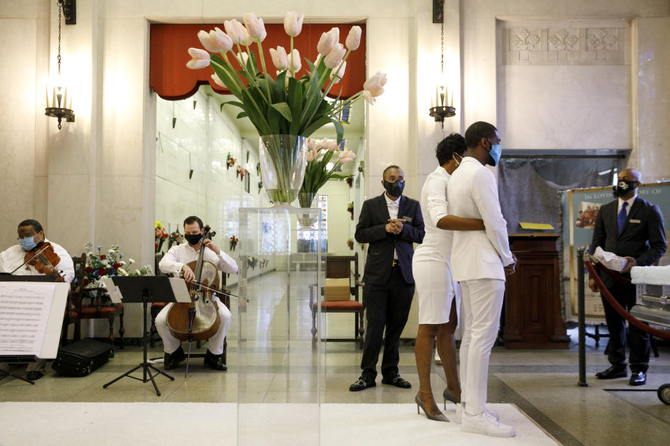 As a masked string quartet plays, Compassion and Serenity Funeral Home Administrator Dani Skinner, center, is present to assist mourners at the viewing of Joanne Paylor, 62, of southwest Washington, during her funeral in Suitland-Silver Hill, Md., Sunday, May 3, 2020. The original funeral for Paylor, who the family believes died of a heart attack, was delayed for close to two months while her family hoped social distancing guidelines would be lifted. When it became clear it would not they decided to proceed and were able to arrange a viewing with only ten people cycling inside at a time from 6 feet apart, and an outdoor service. Despite not having died from coronavirus, almost every aspect of her funeral has been impacted by the pandemic. (AP Photo/Jacquelyn Martin)