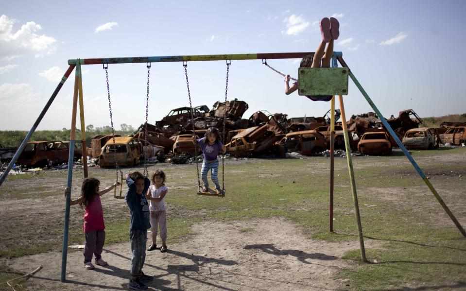 In this Dec. 4, 2013 photo, children play on a swing set backdropped by a chop shop for cars in Buenos Aires, Argentina. Argentines have suffered through a tough summer, with tropical rain that provided no relief from the heat and humidity, people having to throw out rotten food because of rolling power blackouts and soaring oil and gas prices, all amid rising inflation that is making it ever harder to reach the end of the month. The strain is evident on the faces of subway riders and others making their way home in Buenos Aires, where signs of poverty and decay are ubiquitous just beyond the glamorous streets where tourists go. (AP Photo/Rodrigo Abd)